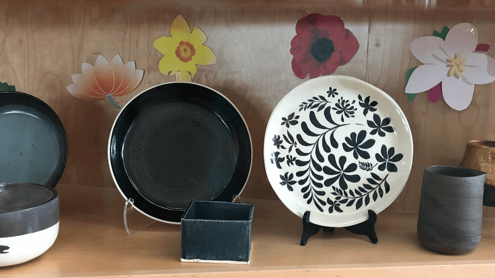 two black and white handmade pottery plates on display. One plate is all black with a white rim, the second plate on the right is white with a floral design.